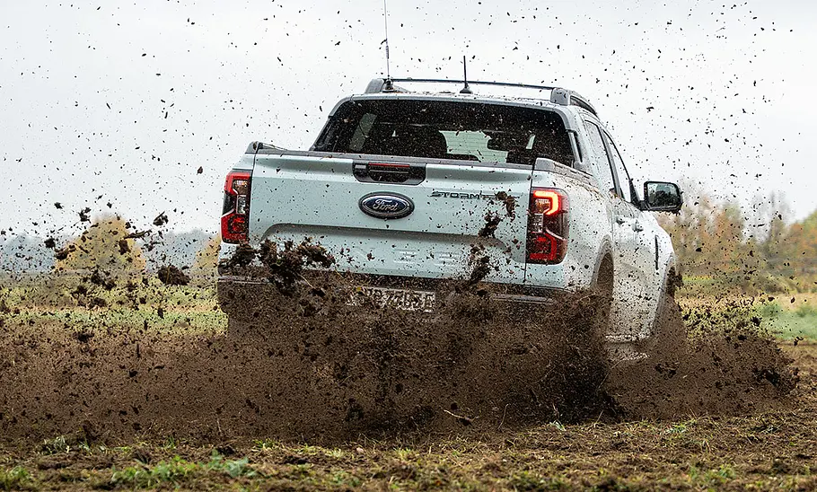 Der Ford Ranger Plug-in-Hybrid (2025) driftet auf einer Weide durch eine Linkskurve und schleudert Erde auf, von hinten fotografiert.