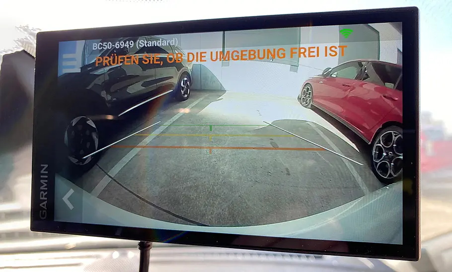 Bildschirm des Garmin DriveSmart 66 MT-S als Rückfahrkamera, fotografiert an der Windschutzscheibe beim Rückwärtseinparken.