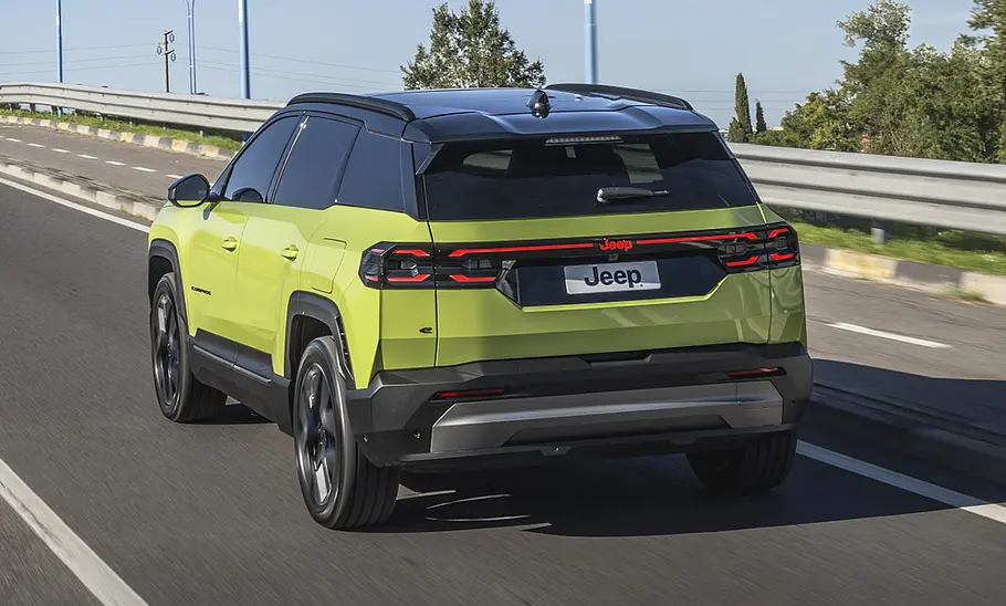 Der Jeep Compass fährt auf einer Straße, von hinten links fotografiert.