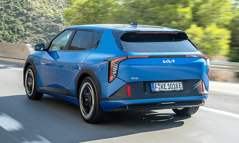 Kia EV4 (2025) Der Kia EV4 (2025) fährt eine Landstraße entlang, von hinten links fotografiert.