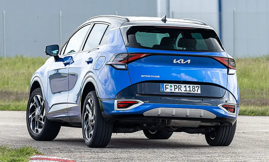 Kia Sportage (2021) Der Kia Sportage (2021) fährt durch eine Linkskurve, von hinten links fotografiert.