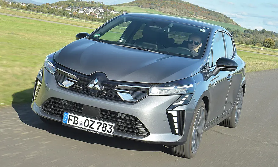Der Mitsubishi Colt Hybrid fährt geradeaus, von vorne links fotografiert.