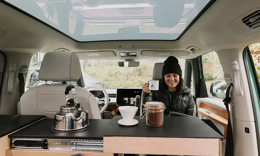 Peace Vans Buzz.Camper Die Küche im Peace Vans Buzz.Camper von der Sitzbank aus gesehen. Eine Person sitzt gegenüber auf dem gedrehten Beifahrersitz.
