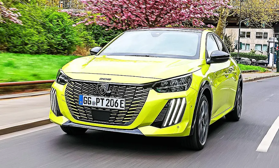 Blick von schräg vorne auf den fahrenden Peugeot E-208.