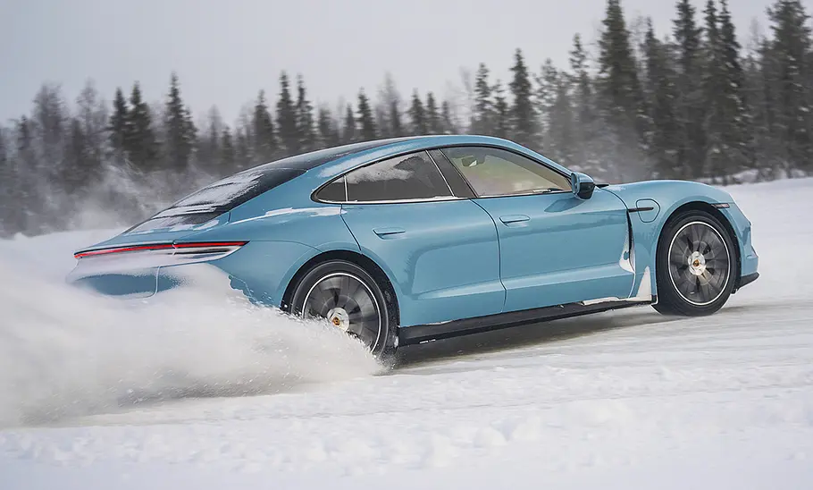 Das Porsche Taycan 4 Facelift (2025) driftet im Schnee durch eine Rechtskurve, von hinten rechts fotografiert.