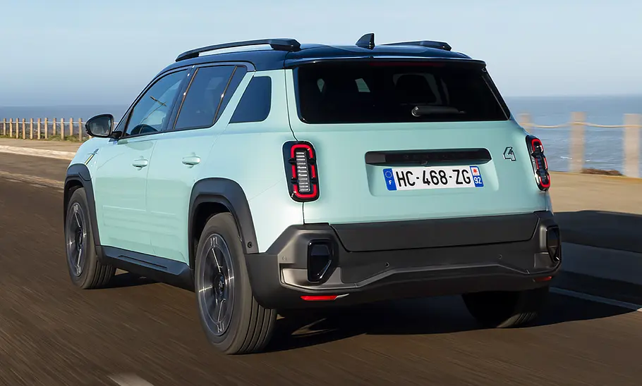 Der Renault 4 E-Tech Electric (2025) fährt eine Küstenstraße entlang, von hinten links fotografiert.