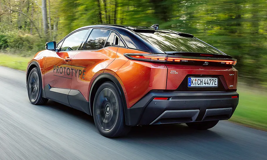 Toyota C-HR+ (2025) Der Toyota C-HR+ (2025) fährt auf einer Landstraße, von hinten links fotografiert.