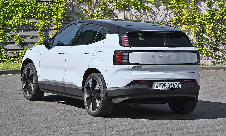 Der Volvo EX30 Single Motor Extended Range Ultra steht vor einer grün bewachsenen Mauer, Ansicht von hinten links.