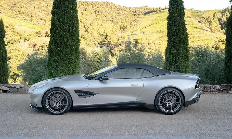 Aston Martin Vanquish Volante (2025) Der Aston Martin Vanquish Volante (2025) steht mit geschlossenem Dach vor einem hügeligen Panorama, von links fotografiert.