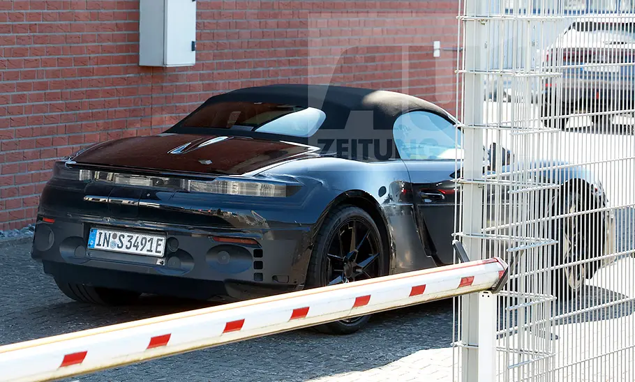 Ein Audi TT-Mule mit der Karosserie eines Porsche 718 fährt über einen Parkplatz, von hinten rechts fotografiert.