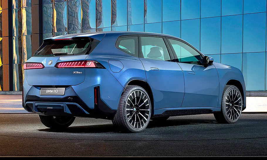 BMW iX3 (2026) Der BMW iX3 (2026) steht vor einer Glasfassade, von hinten rechts fotografiert.