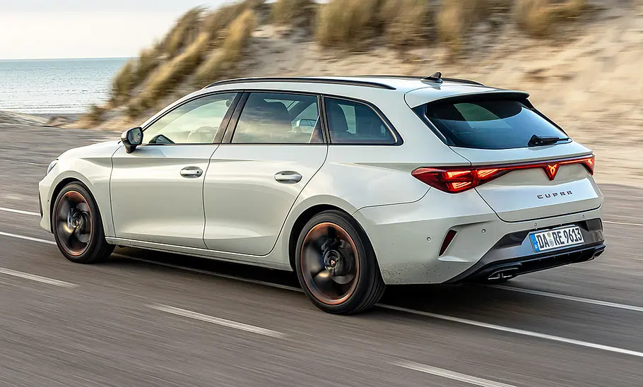 Cupra Leon Sportstourer Der Cupra Leon Sportstourer fährt auf einer Straße an einer Düne entlang, von hinten links fotografiert.