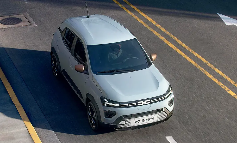 Dacia Spring Facelift (2024) Das Dacia Spring Facelift (2024) fährt durch eine Stadt, von vorne rechts fotografiert.