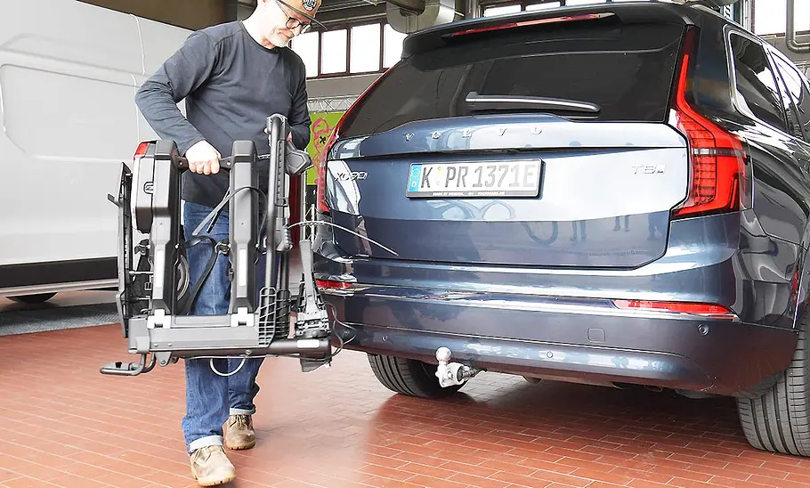 Thule-Fahrradträger für bis zu drei E-Bikes im Test Ein Tester steht am Heck des Testwagens, einem Volvo XC90, und hat den zusammengefalteten Thule-Dahrradträger Easyfold 3 in der Hand.