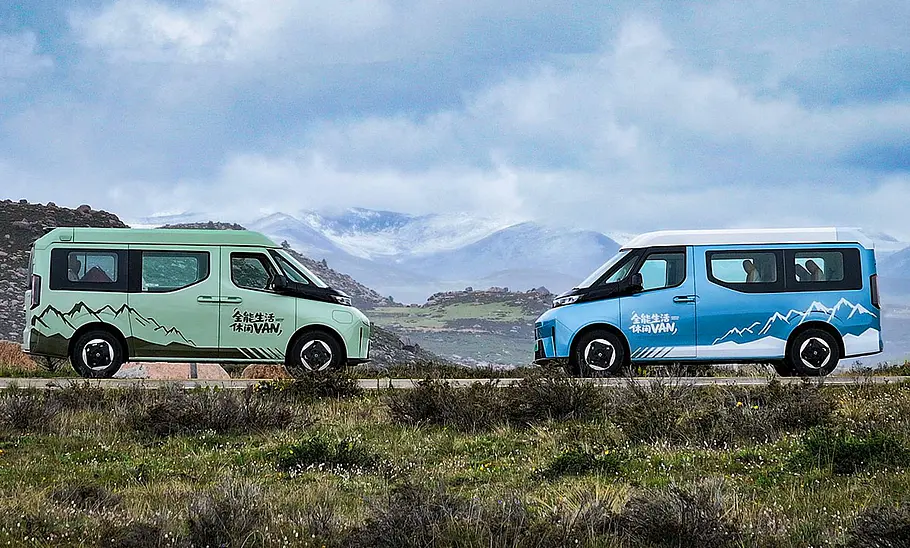 Das Bild zeigt zwei Farizon SV X-Van (2025) statisch der Seite. Links steht ein grüner Van mit der rechten Seite zur Kamera, rechts ein blauer Van mit der linken Seite zur Kamera. Im Hintergrund ist ein Bergpanorama zu sehen.