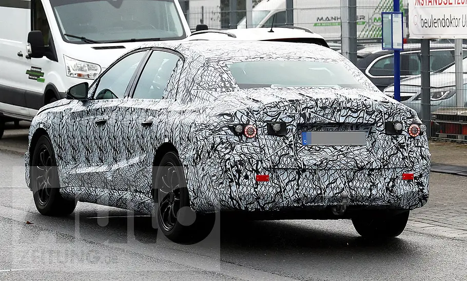 Die Mercedes E-Klasse EQ (2027) fährt als Erlkönig im öffentlichen Straßenverkehr, von hinten links fotografiert.