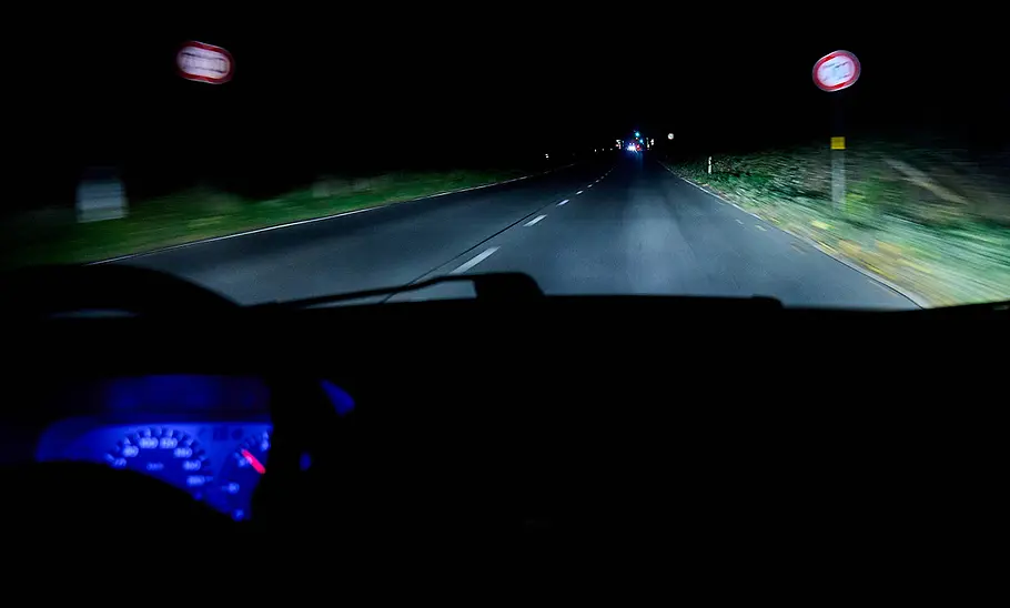 Nächtliche Landstraße, die von einem Auto mit Abblendlicht ausgeleuchtet wird.