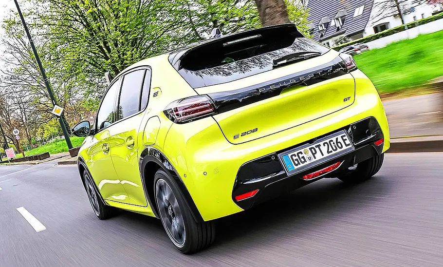 Blick von schräg hinten auf den fahrenden Peugeot E-208.