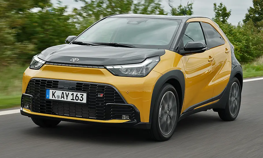 Toyota Aygo X Facelift (2025) fährt auf einer Landstraße, Ansicht von vorne links.
