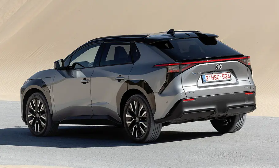 Das Toyota bZ4X Facelift fährt vor einem sandigen Hintergrund, von hinten links fotografiert.