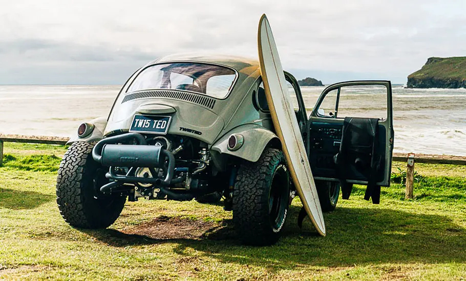 VW Twisted Tbug am Strand mit Surfbrett, fotografiert von hinten.