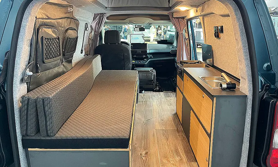 Die Innenaufnahme zeigt den Wohnraum des Alpincamper Peugeot Partner 4x4 (2025) durch die geöffneten Hecktüren.