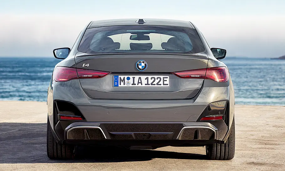 Das BMW i4 Facelift (2024) steht vor einem Küstenpanorama, von hinten fotografiert.