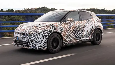 Der Cupra Raval (2026) fährt als Erlkönig über eine Brücke, von vorne links fotografiert. - Foto: Cupra