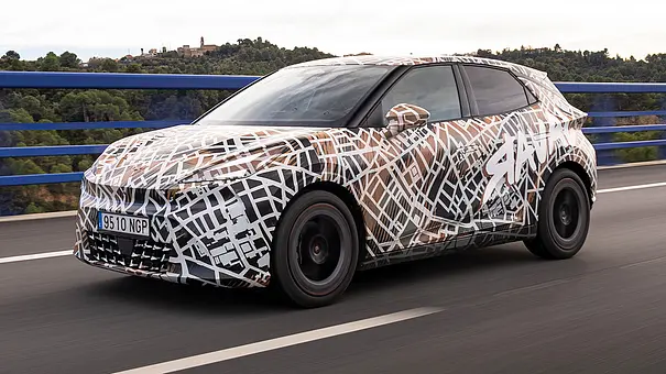 Der Cupra Raval (2026) fährt als Erlkönig über eine Brücke, von vorne links fotografiert. - Foto: Cupra