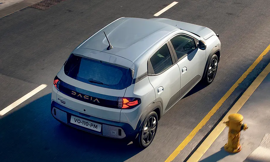 Dacia Spring Facelift (2024) Das Dacia Spring Facelift (2024) fährt durch eine Stadt, von hinten rechts fotografiert.