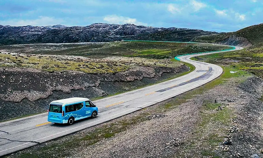 Das Bild zeigt den Farizon SV X-Van (2025) fahrend von schräg hinten rechts. Vor dem Van ist eine kurvige Straße durch eine karge, steinige Landschaft zu sehen.