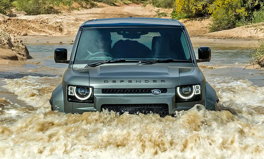 Land Rover Defender Octa (2024) fährt durch einen Fluss, das Wasser reicht bis unter die Frontscheinwerfer, Ansicht von vorne.
