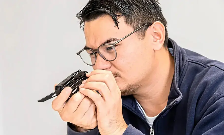 Prüfer beim Sichttest der Säge eines Multitools, fotografiert von der Seite.