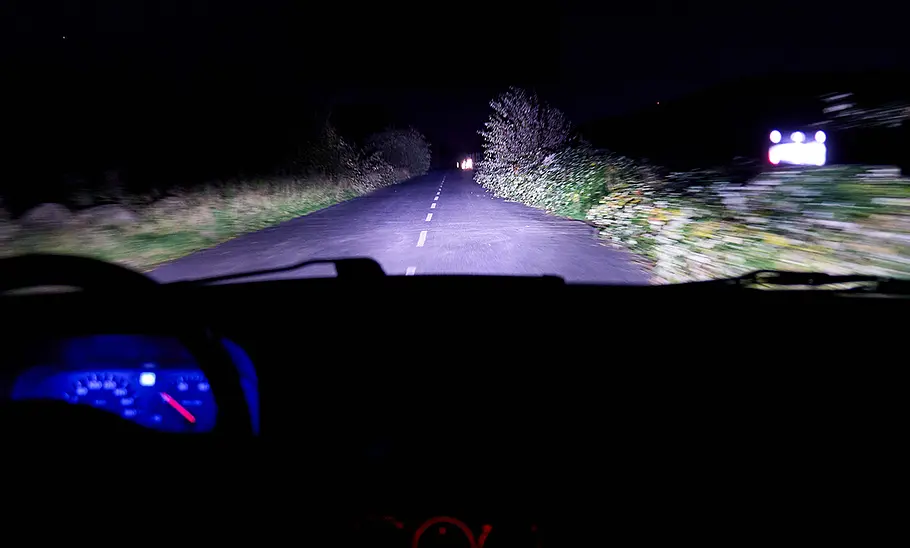 Nächtliche Landstraße, die von einem Auto mit Fernlicht ausgeleuchtet wird.