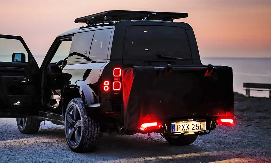 Thule Outset (2024) Das montierte Thule Outset (2024) zusammengeklappt am Auto montiert. Das Fahrzeug steht auf einem Parkplatz, im Hintergrund das Meer in der Dämmerung.