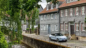 Der Volvo EX30 steht vor einem alten Gebäude in Goslar, davor fließt wenige Meter tiefer ein kleiner Fluss. - Foto: Frank Ratering