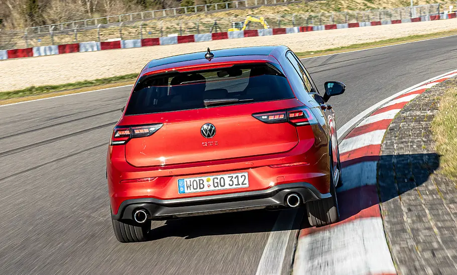 Der VW Golf GTI fährt auf der Grand-Prix-Strecke des Nürburgring durch eine Rechtskurve, von hinten fotografiert.