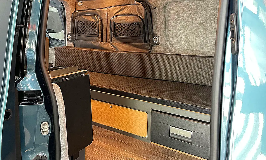 Alpincamper Peugeot Partner 4x4 (2025) Die Innenaufnahme zeigt die Sitzbank des Alpincamper Peugeot Partner 4x4 (2025) durch die geöffnete Schiebetüre.