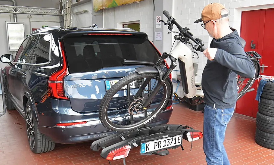 Thule-Fahrradträger für bis zu drei E-Bikes im Test Ein Tester hebt ein E-Bike auf den am Testwagen montierten Heckträger.