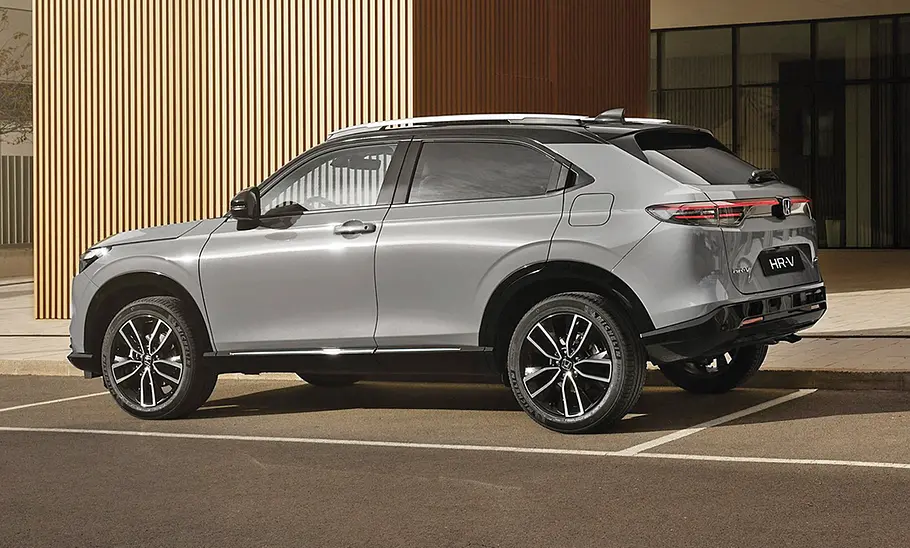 Honda HR-V Facelift (2025) steht auf einem Parkplatz vor einem Gebäude. Ansicht von hinten links.