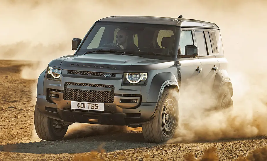 Land Rover Defender Octa (2024) fährt im Gelände und wirbelt Staub auf. Ansicht von vorne links.