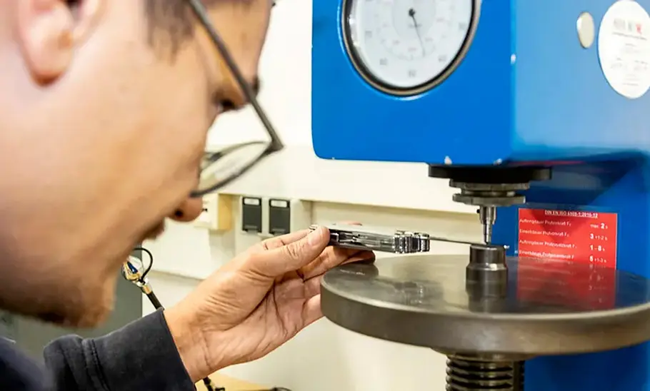 Prüfer beim Testen der Materialhärte eines Multitools, fotografiert von hinten.