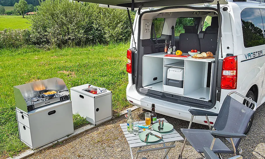 Pössl Vanster Das Bild zeigt die Campingbox Kitchen des Pössl Vanster im Detail. Vor der geöffneten Heckklappe stehen Campingmöbel.