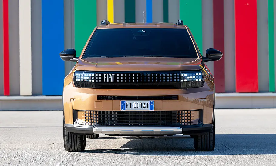 Der Fiat Grande Panda Hybrid (2025) steht vor einer bunt eingefärbten Wand, von vorne fotografiert.
