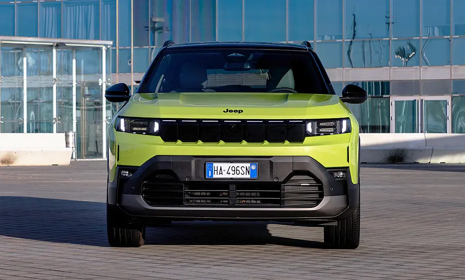 Der Jeep Compass steht vor einer verglasten Fassade, von vorne fotografiert.