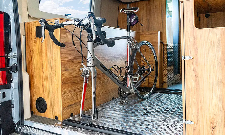 Karmann Dexter 635 (2025) Das Bild zeigt ein Fahrrad im Laderaum unter dem hochgefahrenen Heckbett des Karmann Dexter 635 (2025).