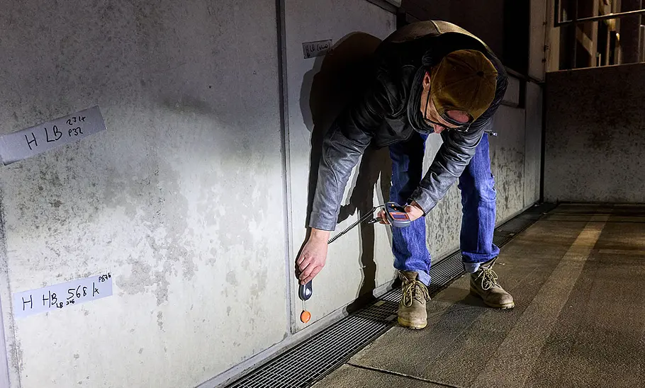 Tester beim Messen der Lichtstärke mit Luxmeter vor der Messwand.