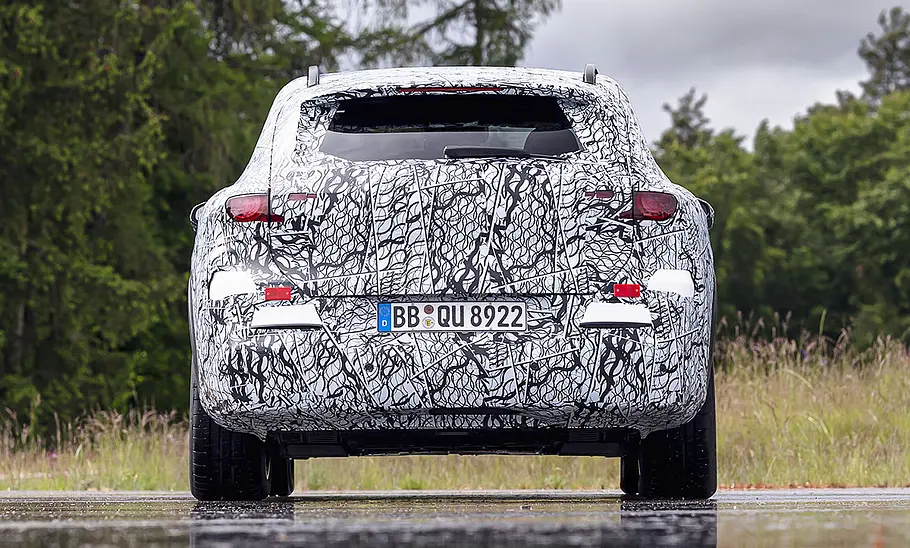 Der Mercedes GLC EQ (2026) steht als Erlkönig auf einem nassen Parkplatz, von hinten fotografiert.