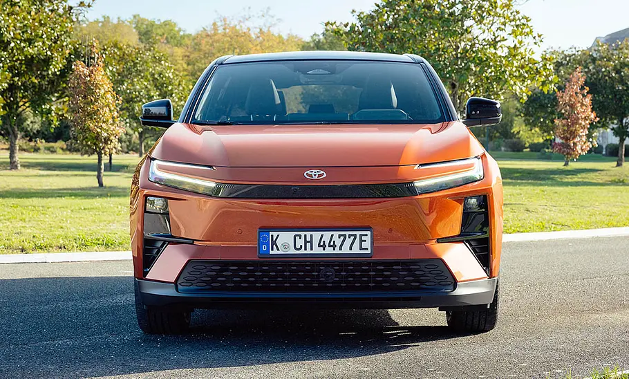Toyota C-HR+ (2025) Der Toyota C-HR+ (2025) steht auf einer Straße im Grünen, von vorne fotografiert.