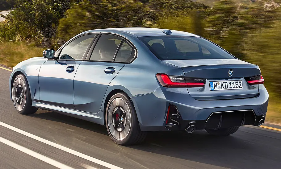 Das BMW 3er Facelift (2024) fährt auf einer Landstraße, von hinten links fotografiert.